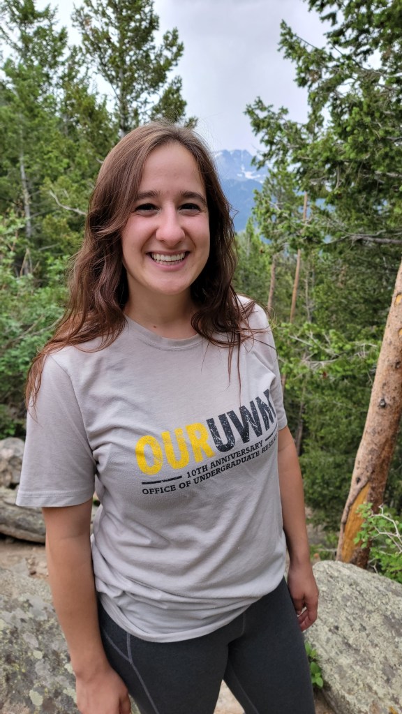 Photograph of archivist Nora Plant wearing OurUWM t-shirt with forest in the background.