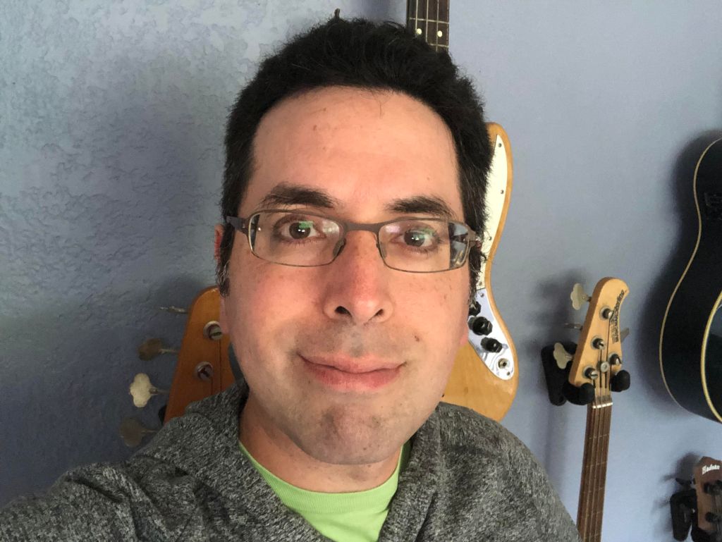 Headshot of Erik R. Bauer, with guitars hanging on the wall